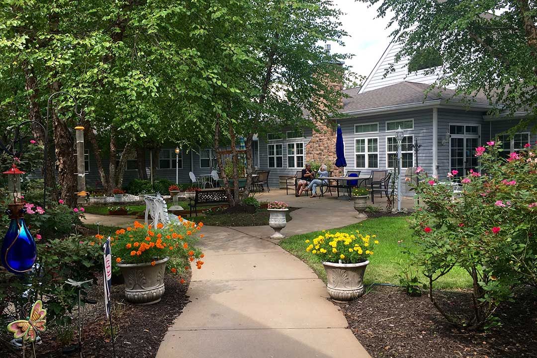 A serene garden pathway leading to a cozy patio area surrounded by lush greenery.