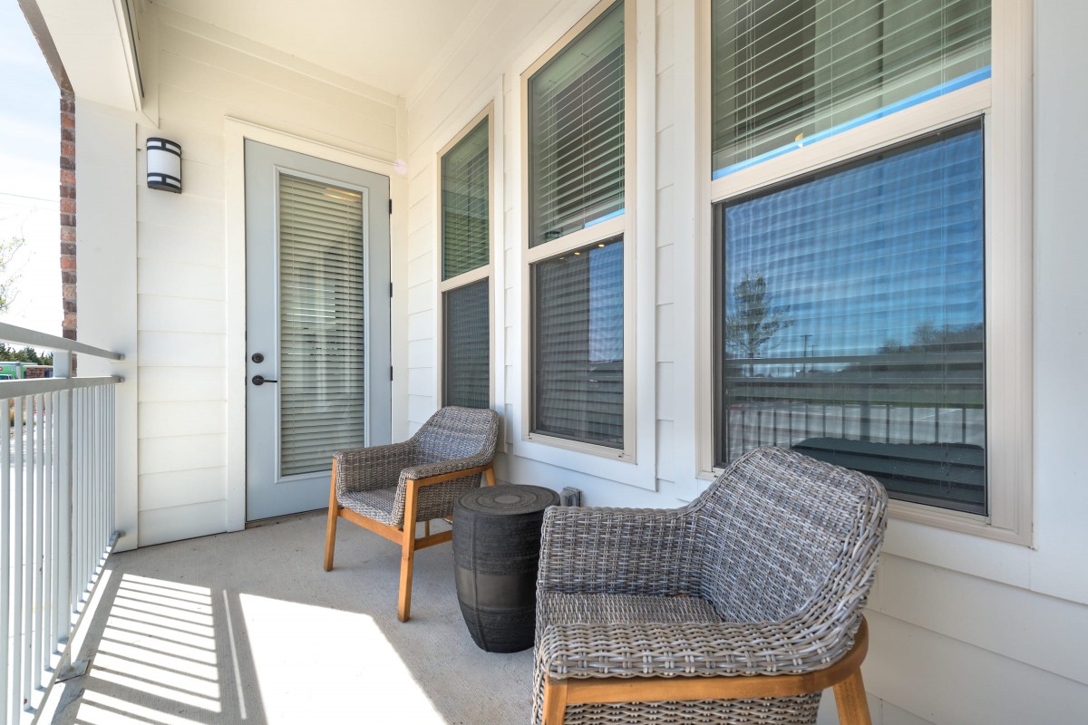 A cozy patio with two woven chairs and a small table next to large windows.