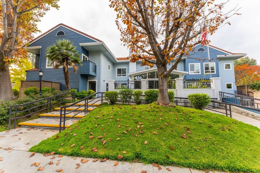 A two-story residential building with a well-maintained lawn and trees in the foreground.