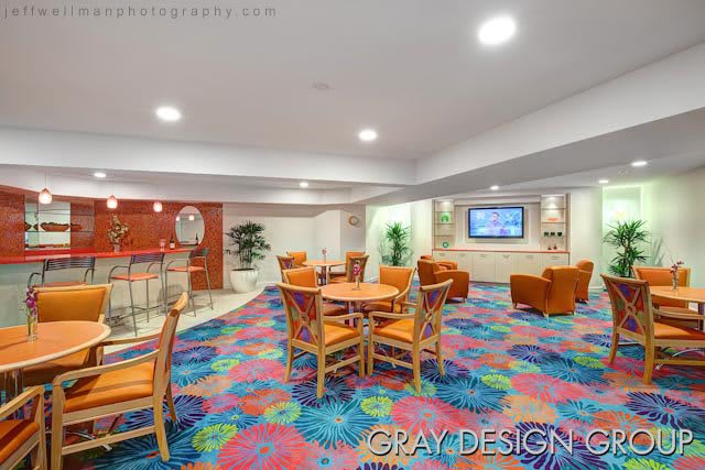 A vibrant lounge featuring a colorful carpet, seating areas with tables and chairs, and a bar section.