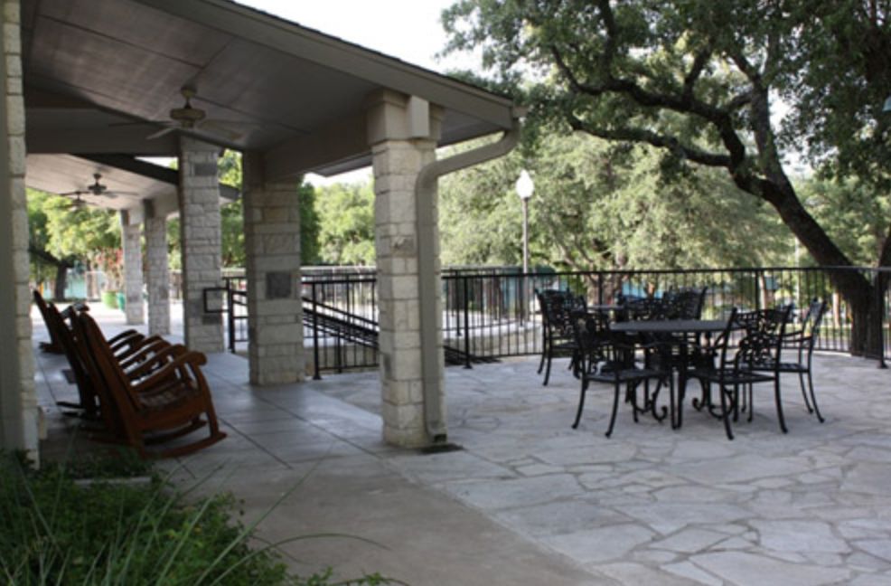 An inviting outdoor patio with seating under a covered area, surrounded by trees.