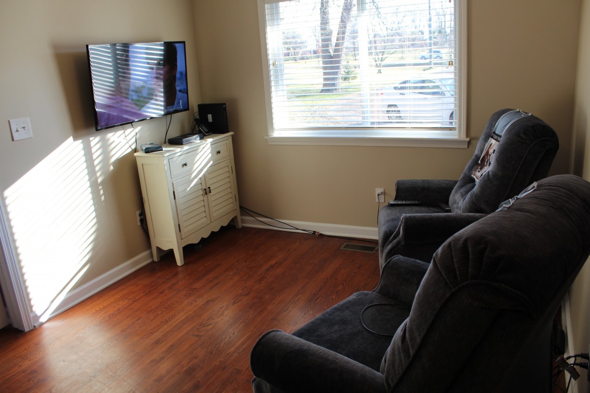 A cozy living room with armchairs facing a television and a window with blinds.