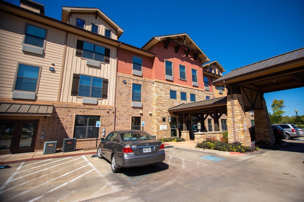 A hotel building with a car parked in the adjacent parking lot on a sunny day.