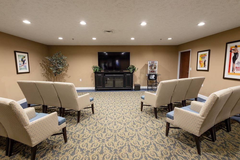 A cozy seating area with chairs arranged facing a large TV, in a carpeted room.