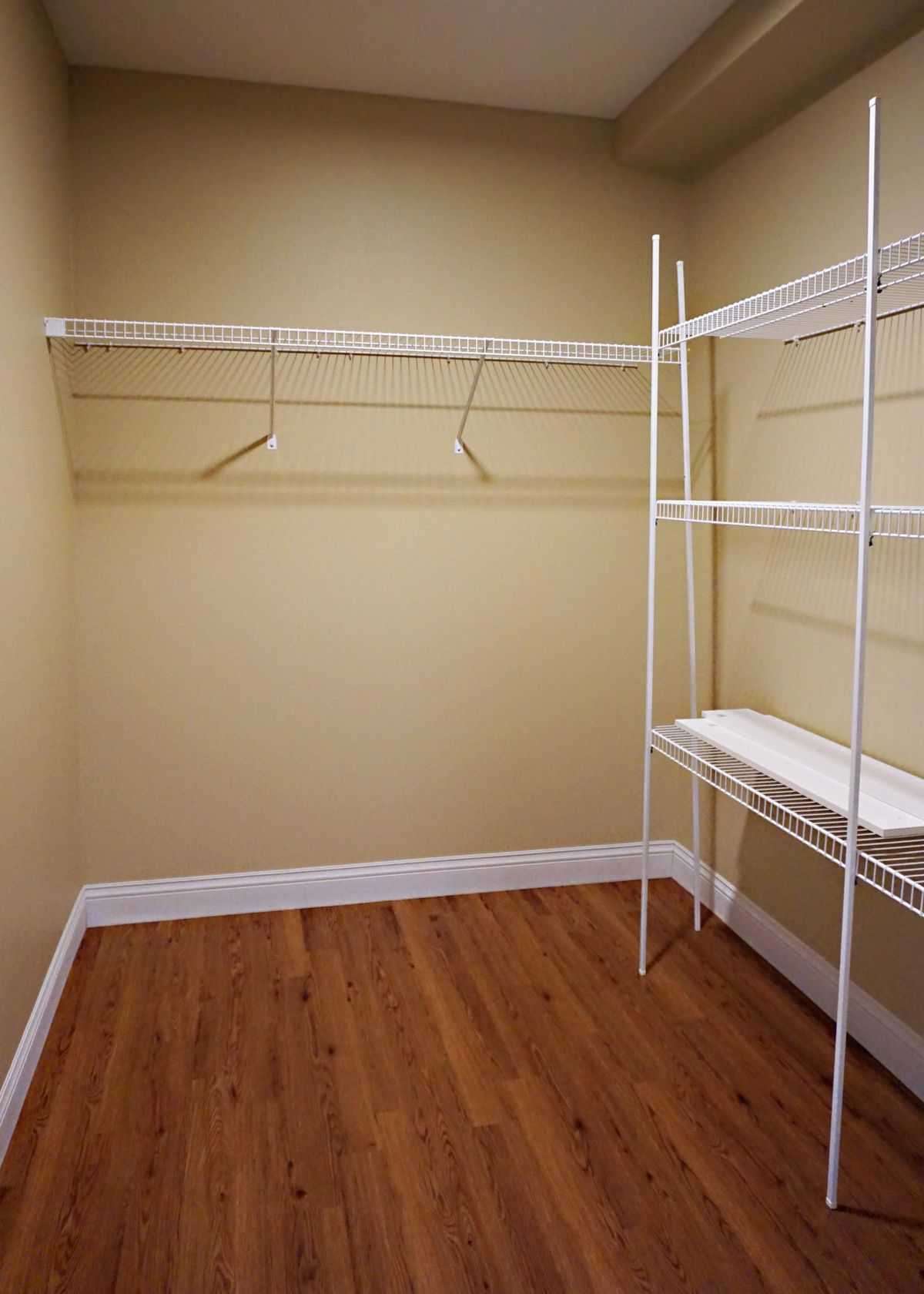 An empty closet with wire shelving and hangers, featuring wood flooring and beige walls.