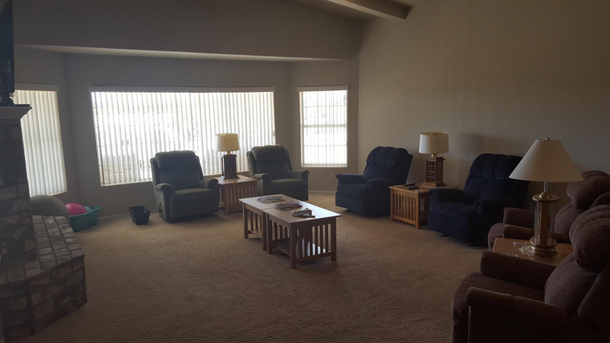 A cozy living room with comfortable chairs and a coffee table, warmly lit by lamps near the windows.