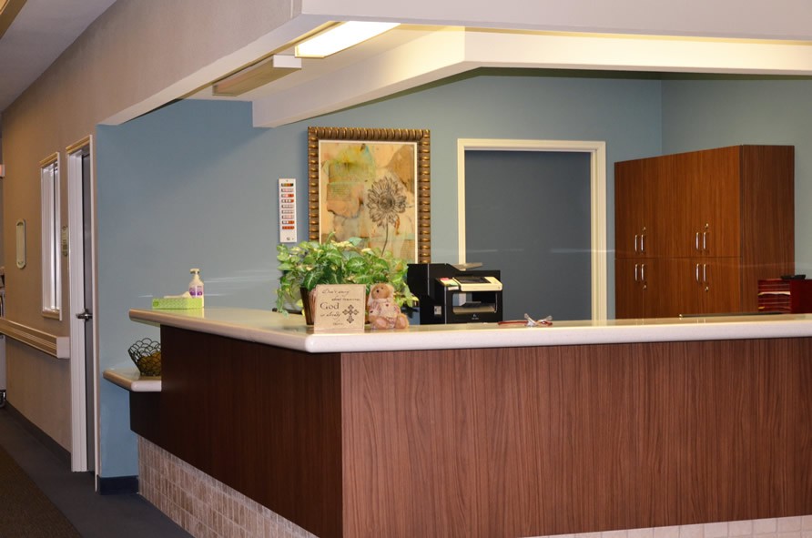 An office reception area with a wooden counter, a plant, and a printer.