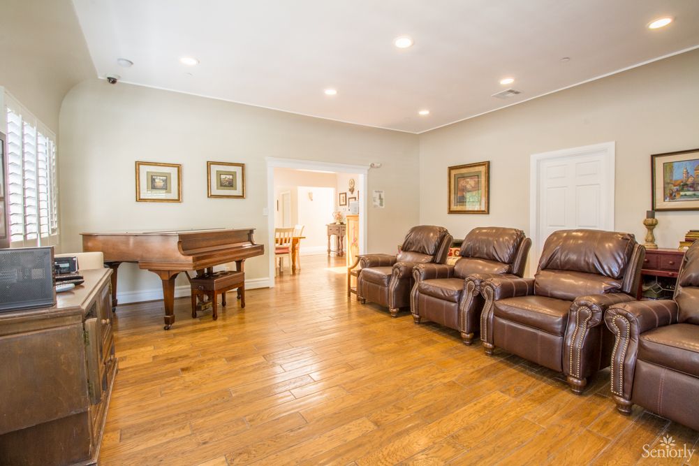 A spacious living room featuring hardwood floors, a grand piano, and comfortable recliner chairs.