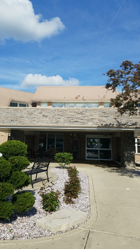 A modern building with a stone facade, surrounded by well-kept landscaping and benches.