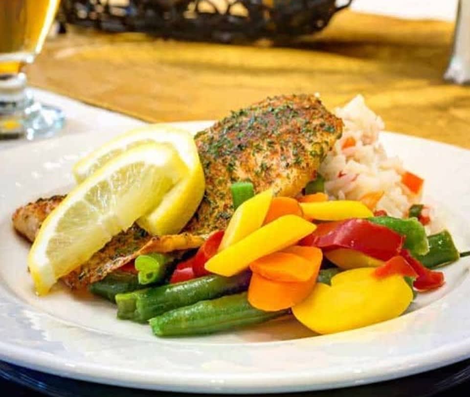 A plate of seasoned salmon served with colorful mixed vegetables and lemon slices.