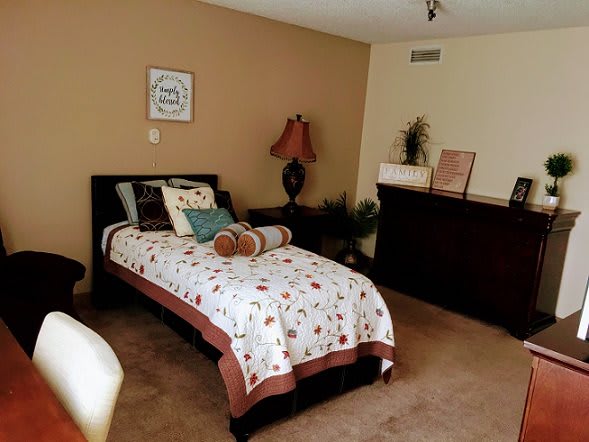 A cozy bedroom with a single bed, decorated with floral bedding and pillows, alongside a lamp and dresser.