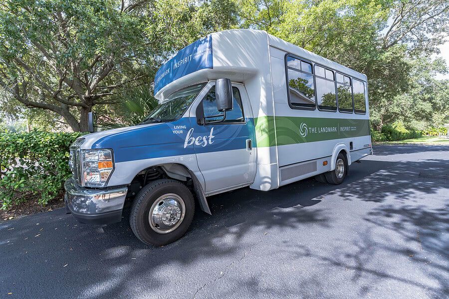 A blue and green shuttle bus parked on a sunny street surrounded by trees.