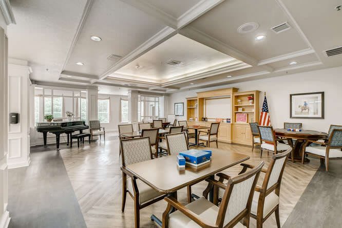 A spacious and well-lit meeting room with tables, chairs, bookshelves, and an American flag, featuring a board game on one table.