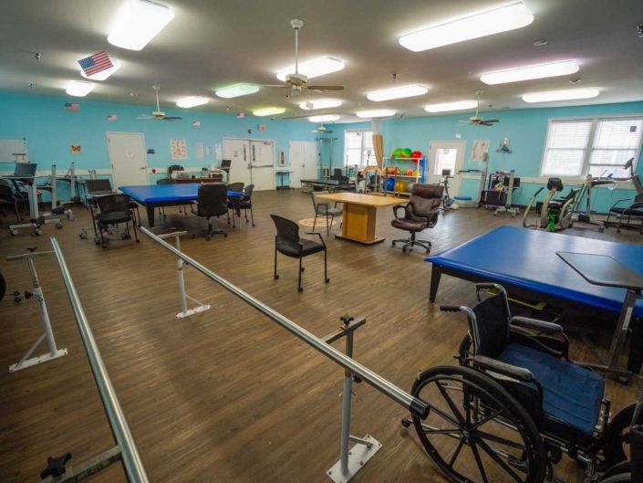 A rehabilitation center room equipped with therapy tables, wheelchairs, and parallel bars for physical therapy exercises.