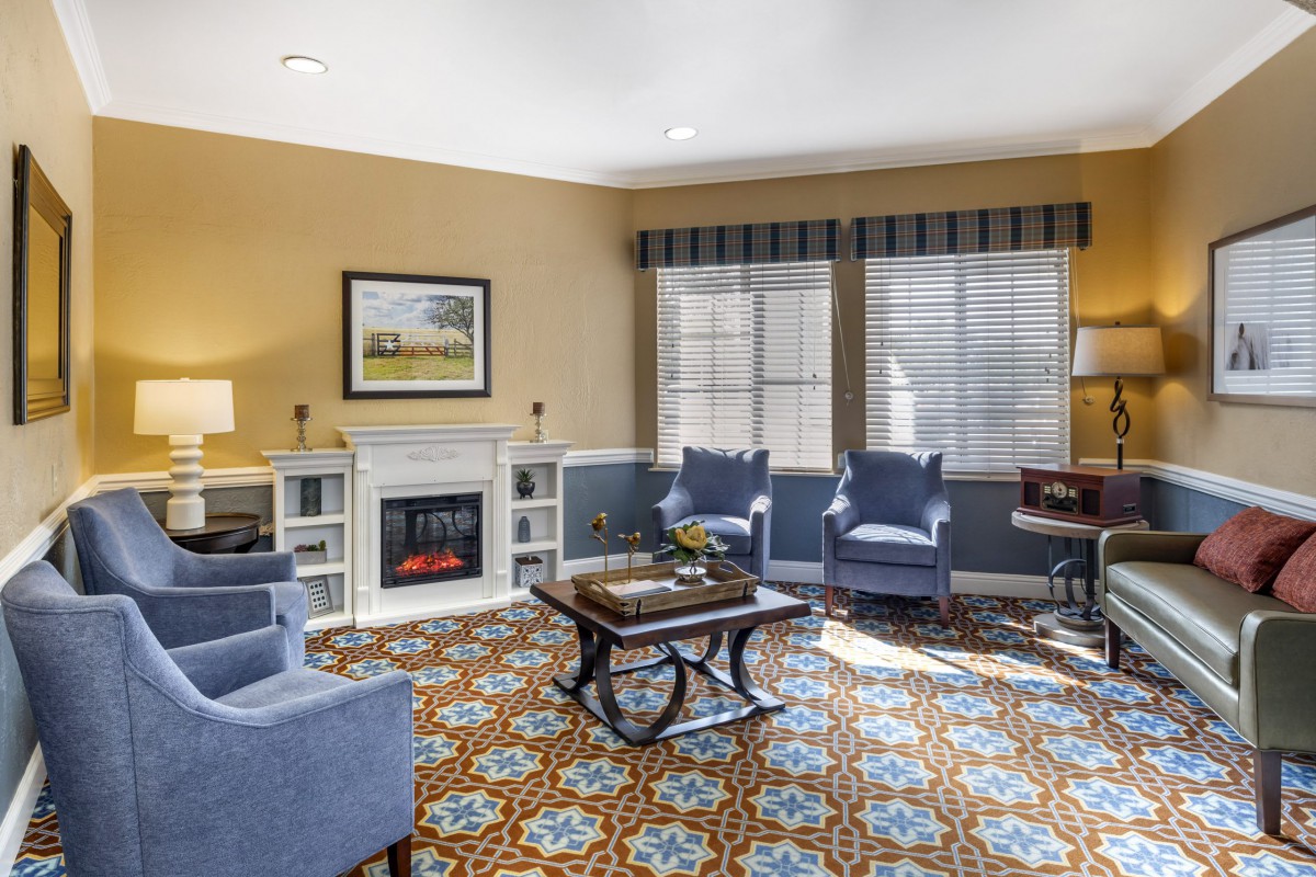 A cozy living room featuring blue chairs, a fireplace, and a patterned carpet.