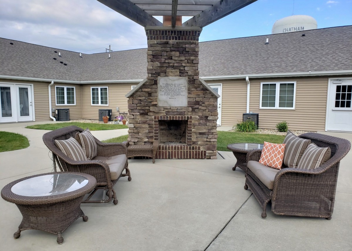 An outdoor patio setting with wicker furniture and a brick fireplace, situated near a building.