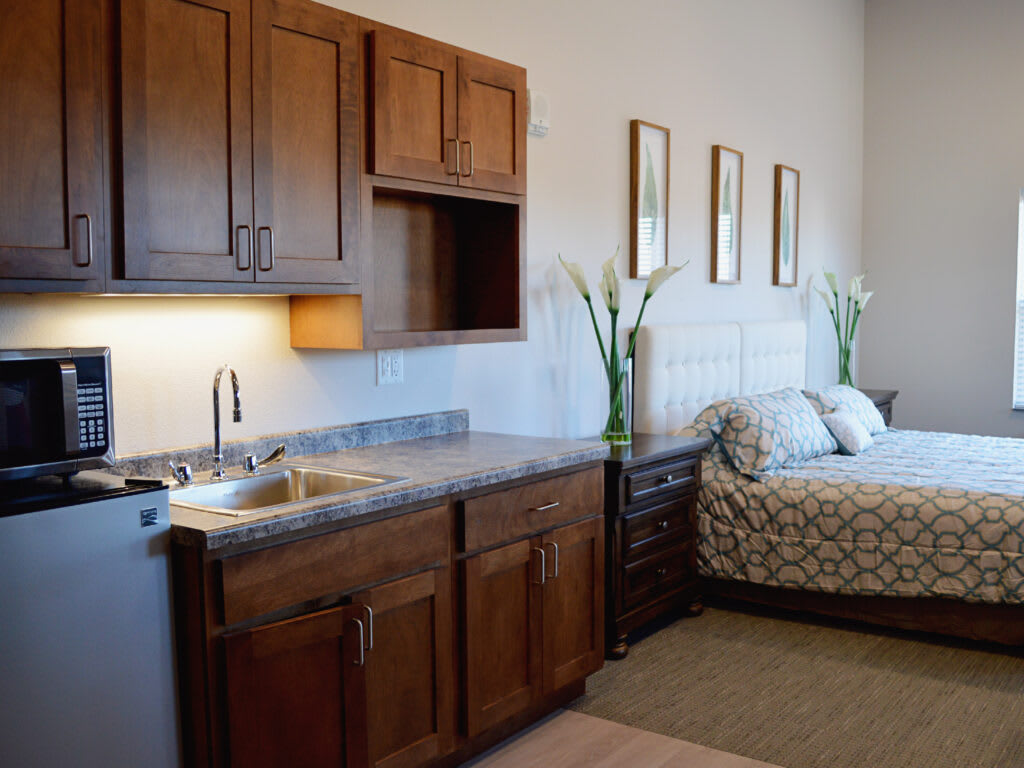 A cozy room featuring a small kitchenette with wooden cabinets and a comfortable bed.