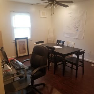 A home office with a desk, chair, and table set up near a window.