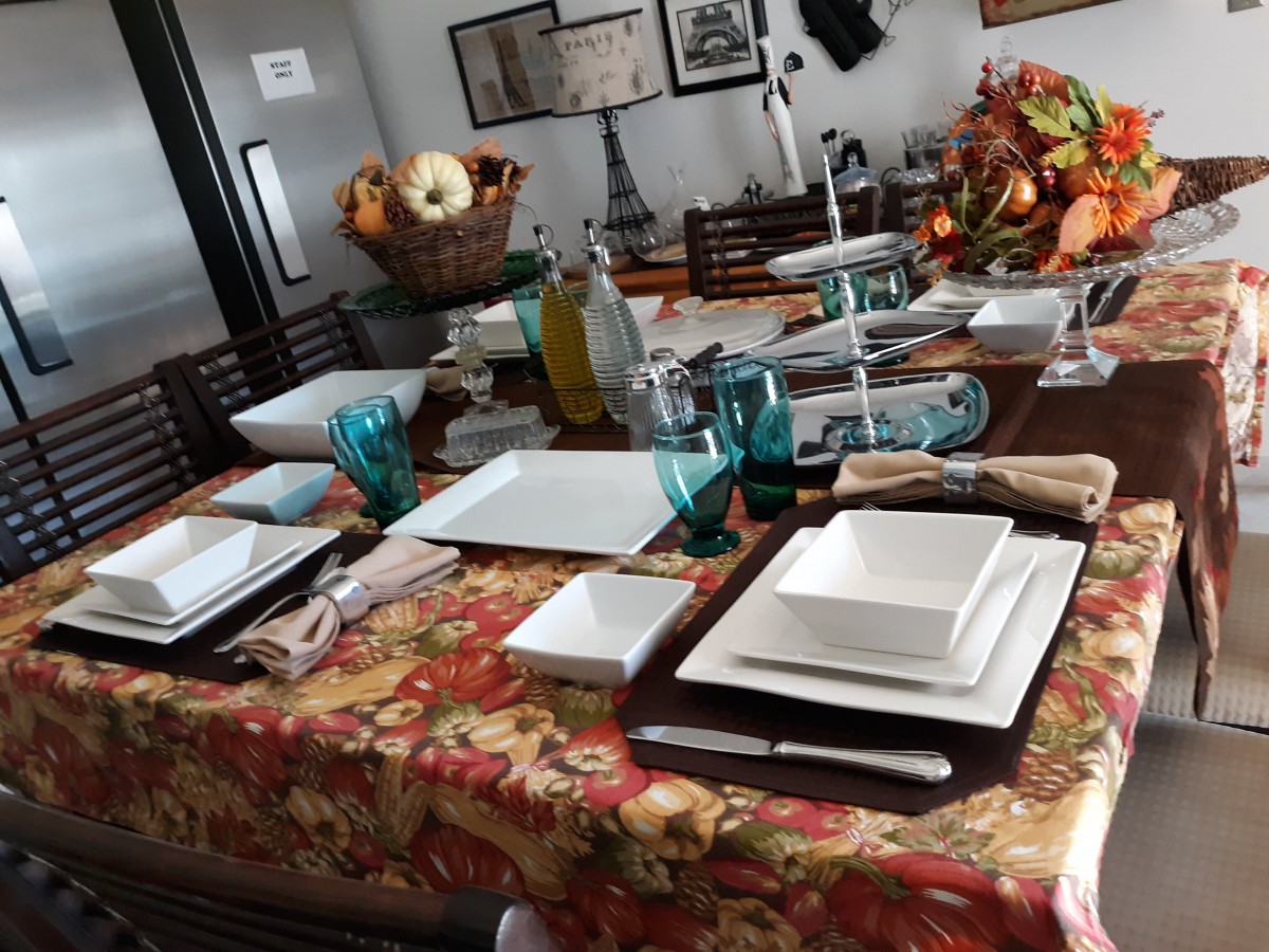 A beautifully set dining table with square plates, blue glasses, and fall-themed decorations.