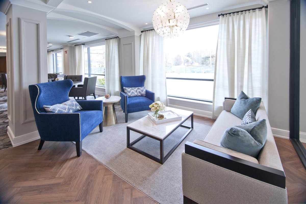 A modern living room featuring elegant blue chairs, a sleek coffee table, and bright lighting from a chandelier.