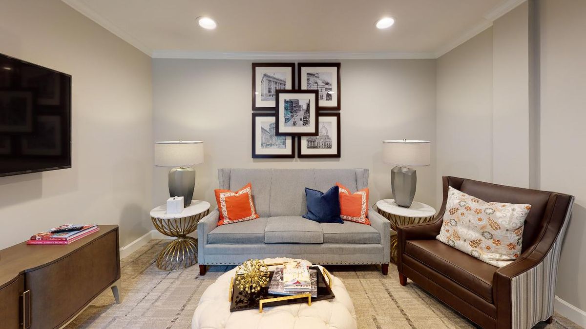 A cozy living room with a modern gray sofa, accented by colorful cushions and flanked by stylish lamps. A set of framed pictures adorns the wall above.