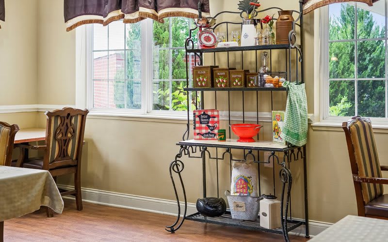 A kitchen corner with a decorative metal shelf unit, filled with various kitchen items and bathed in natural light from a nearby window.