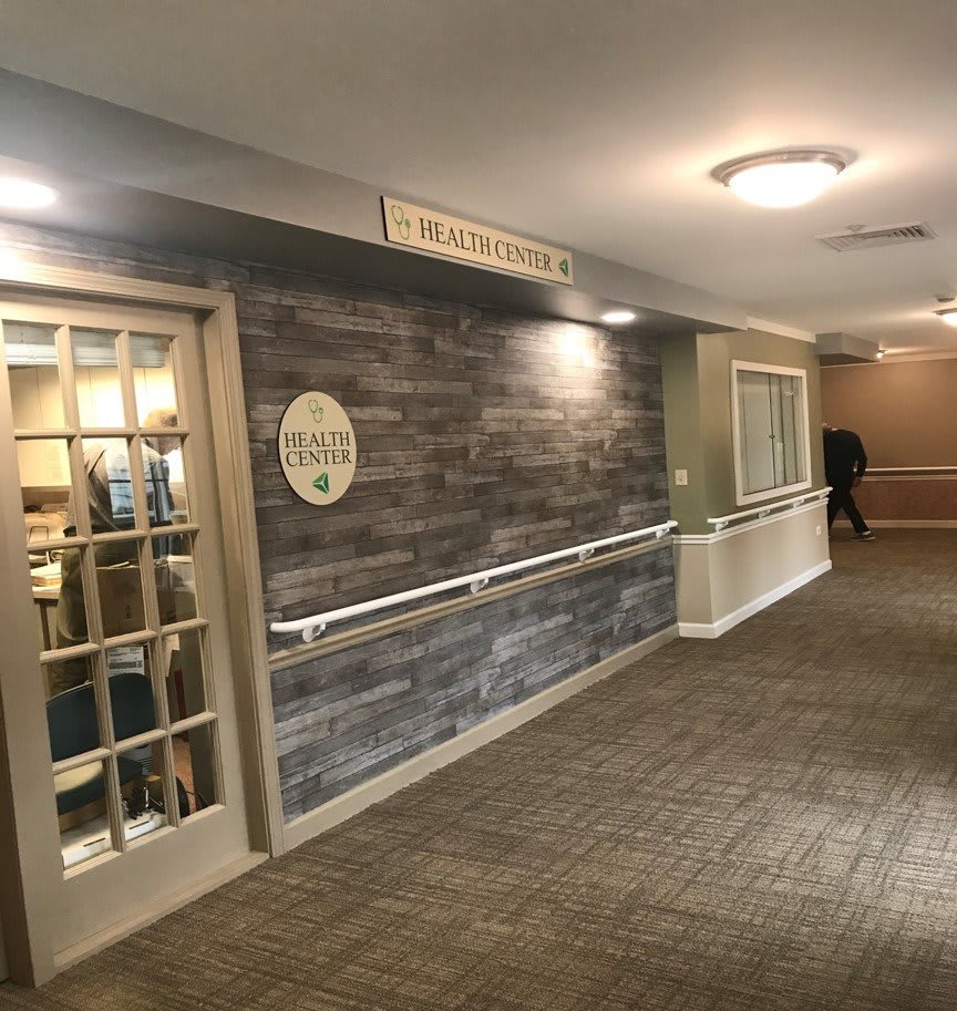 A well-lit hallway with a wooden door, handrails, and signage on the wall.