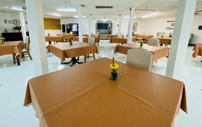 An empty dining hall with tables covered in brown tablecloths and a small centerpiece on each table.