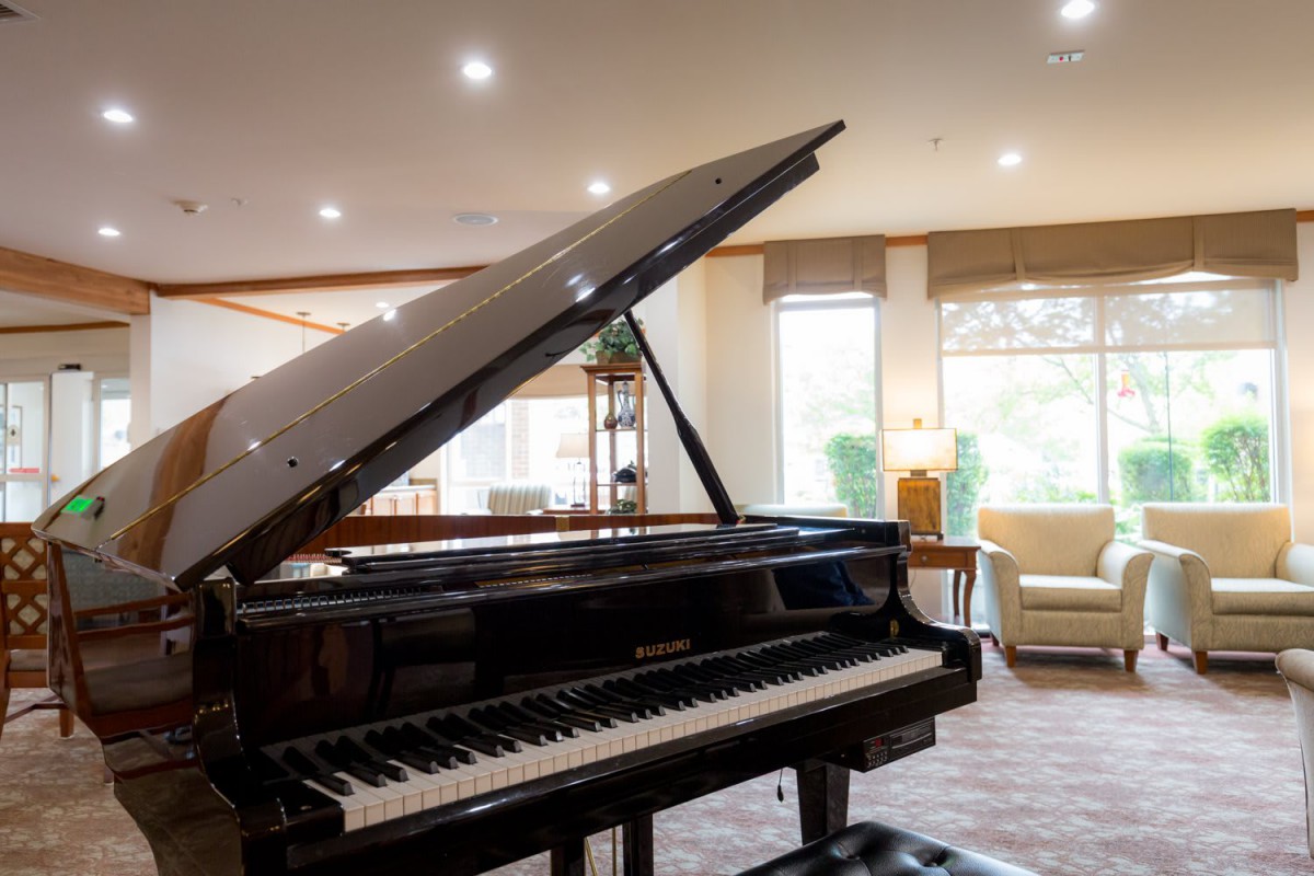 A grand piano in a well-lit music room with large windows and comfortable seating.