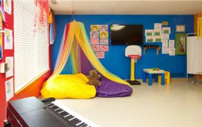 A colorful children's playroom with a rainbow canopy, comfortable beanbags, educational posters, and various activities.