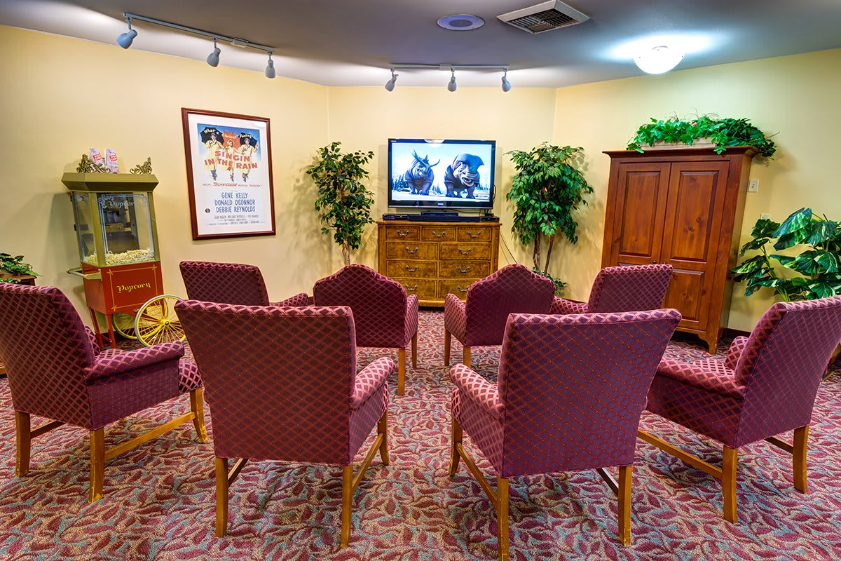 A cozy meeting room with chairs arranged around a television, surrounded by plants and decorated with wall art.