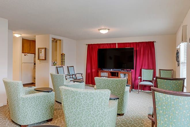 A cozy living room with a television, chairs, and red curtains.