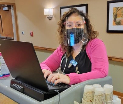 A healthcare worker using a laptop while wearing safety gear, including a mask and face shield.
