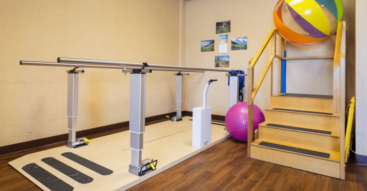 A rehabilitation gym with parallel bars, an exercise ball, and a staircase for physical therapy exercises.