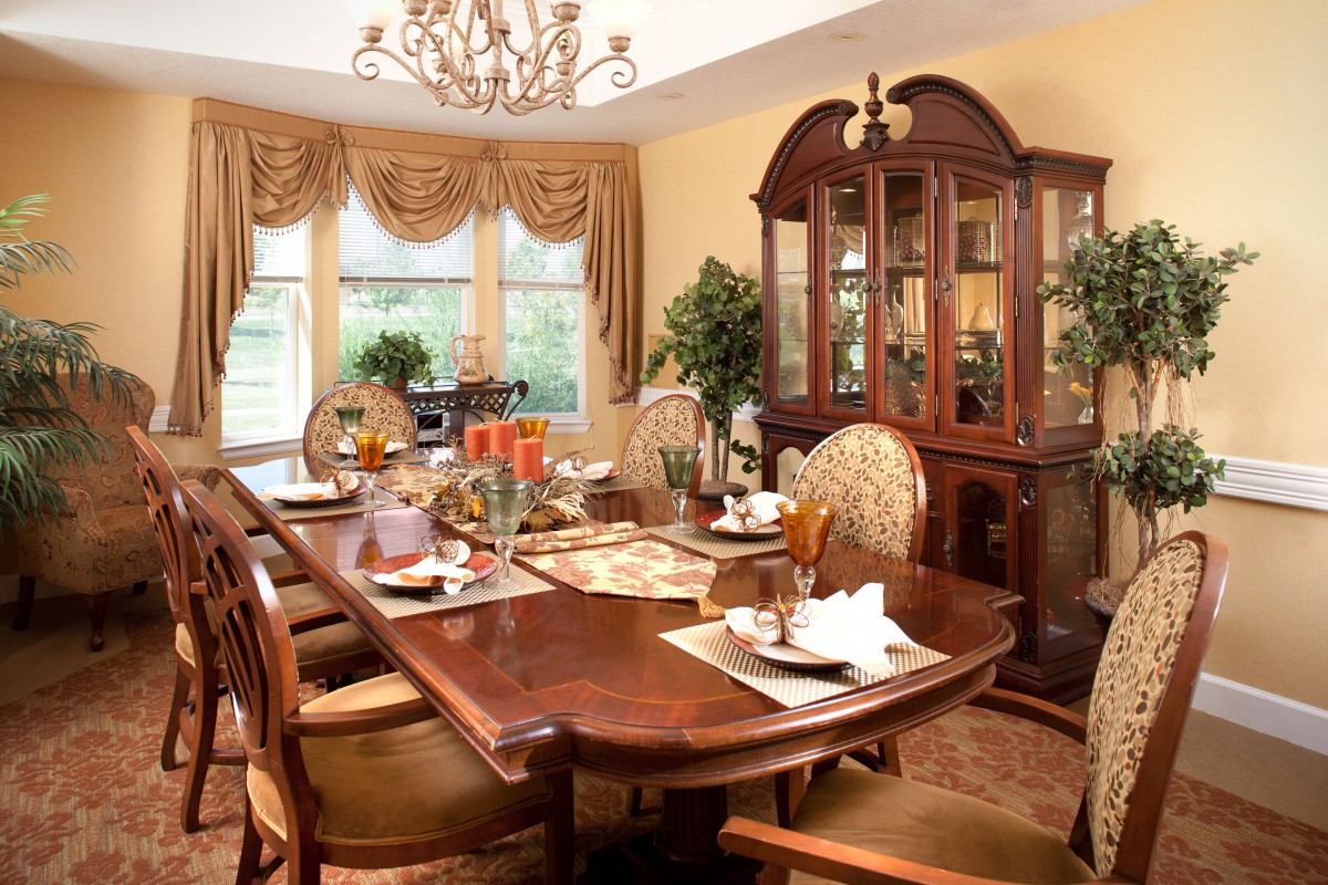 An elegantly furnished dining room with a large wooden table set for a meal, surrounded by ornate chairs and illuminated by a chandelier.