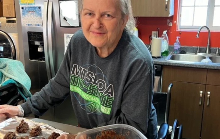 A person smiling in a kitchen while preparing food.