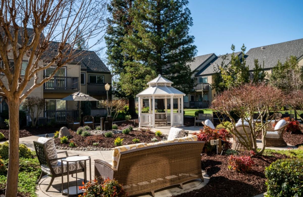A serene outdoor garden with a white gazebo surrounded by patio furniture and landscaping.