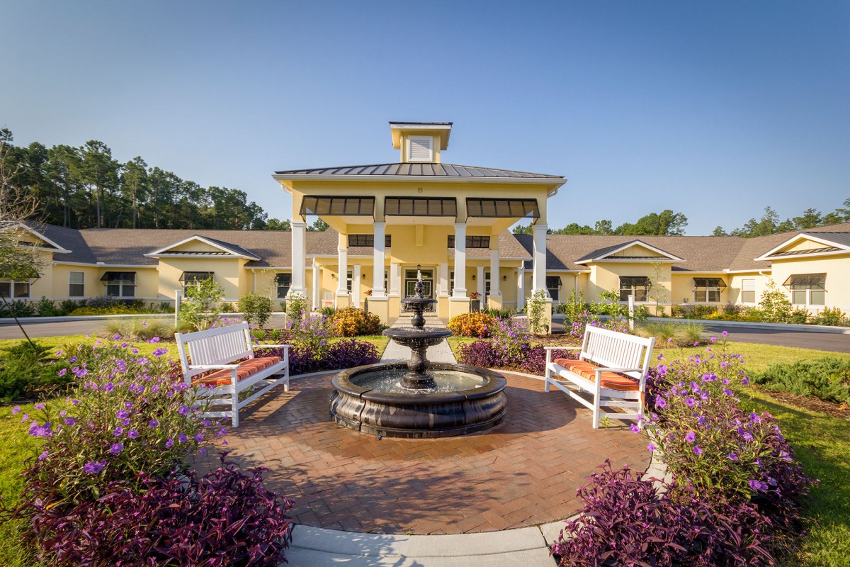 A beautifully landscaped area in front of a building featuring a fountain and benches.