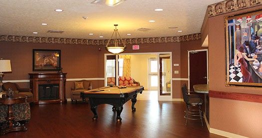 A cozy billiard room featuring a pool table, elegant chandelier, and comfortable seating on wooden floors.