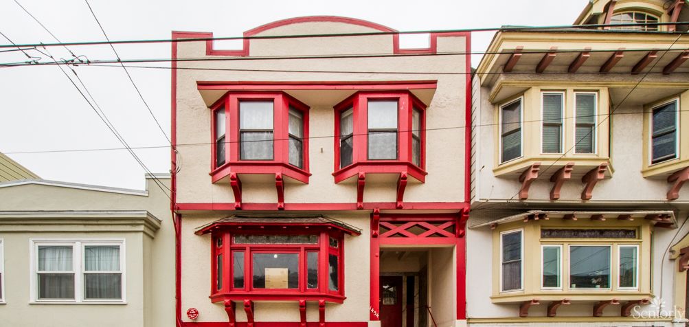 A two-story residential building with prominent red-trimmed bay windows.