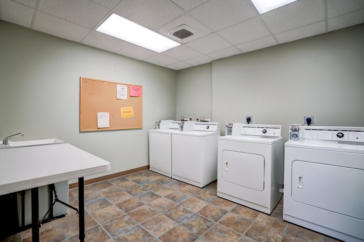 A clean laundry room featuring several washing machines and dryers, with a bulletin board on the wall.