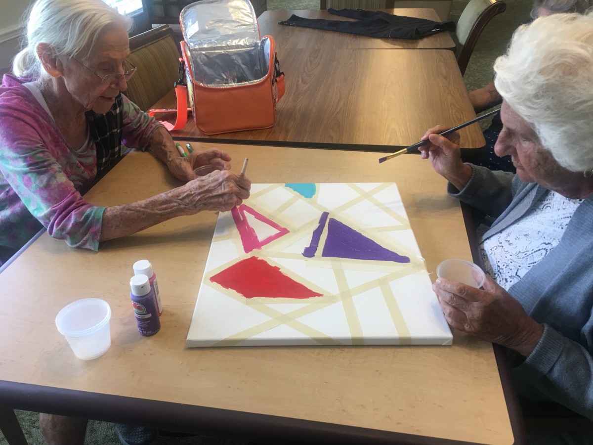 Two seniors engaged in a collaborative painting project using colorful geometric shapes.