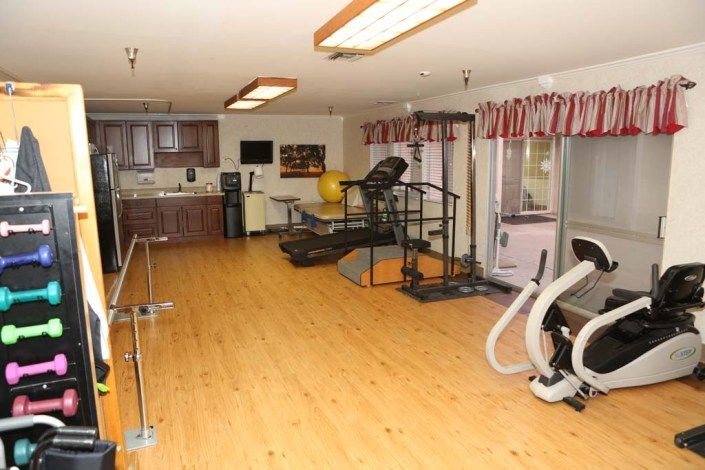 A well-equipped gym room with various exercise machines and a wooden floor.