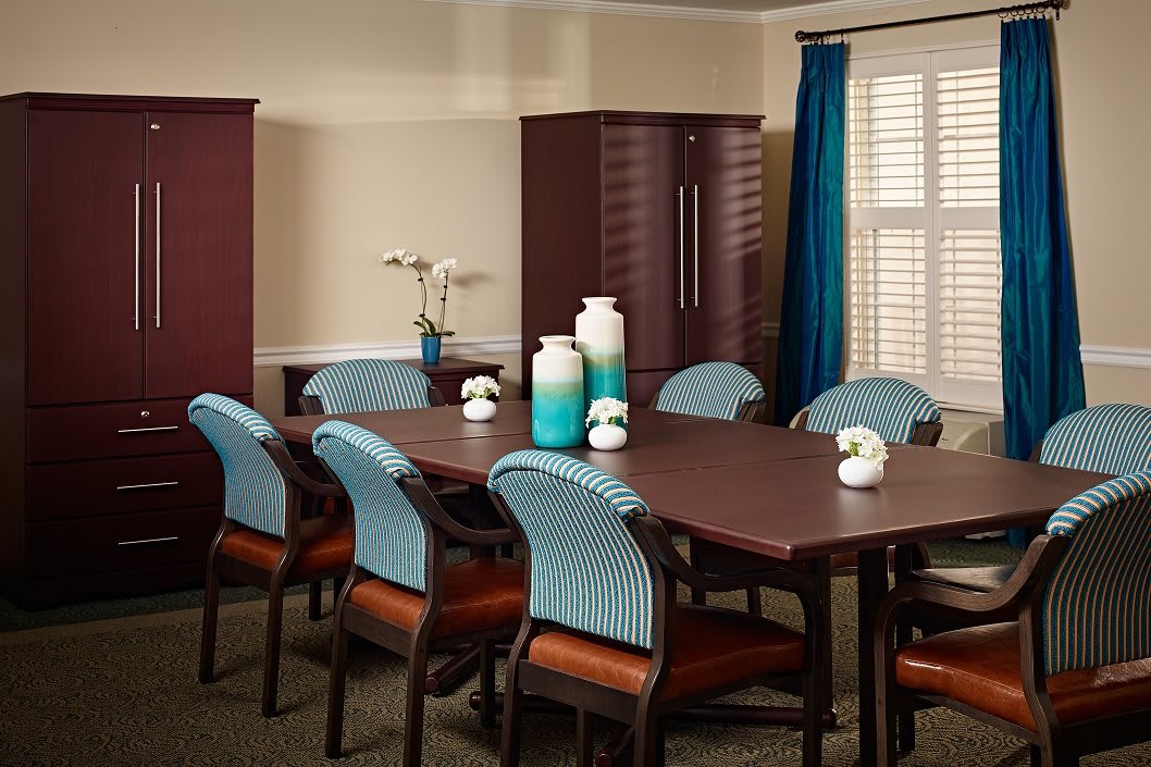 A well-organized conference room with a long meeting table, surrounded by chairs and decorated with vases and window curtains.