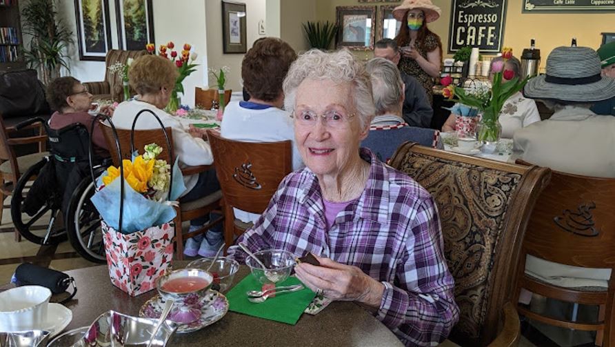 An elderly woman enjoying tea at a social gathering in a cafe setting.