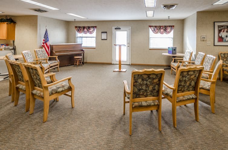 A small meeting room with chairs arranged in a circle, featuring a podium, piano, and an American flag.
