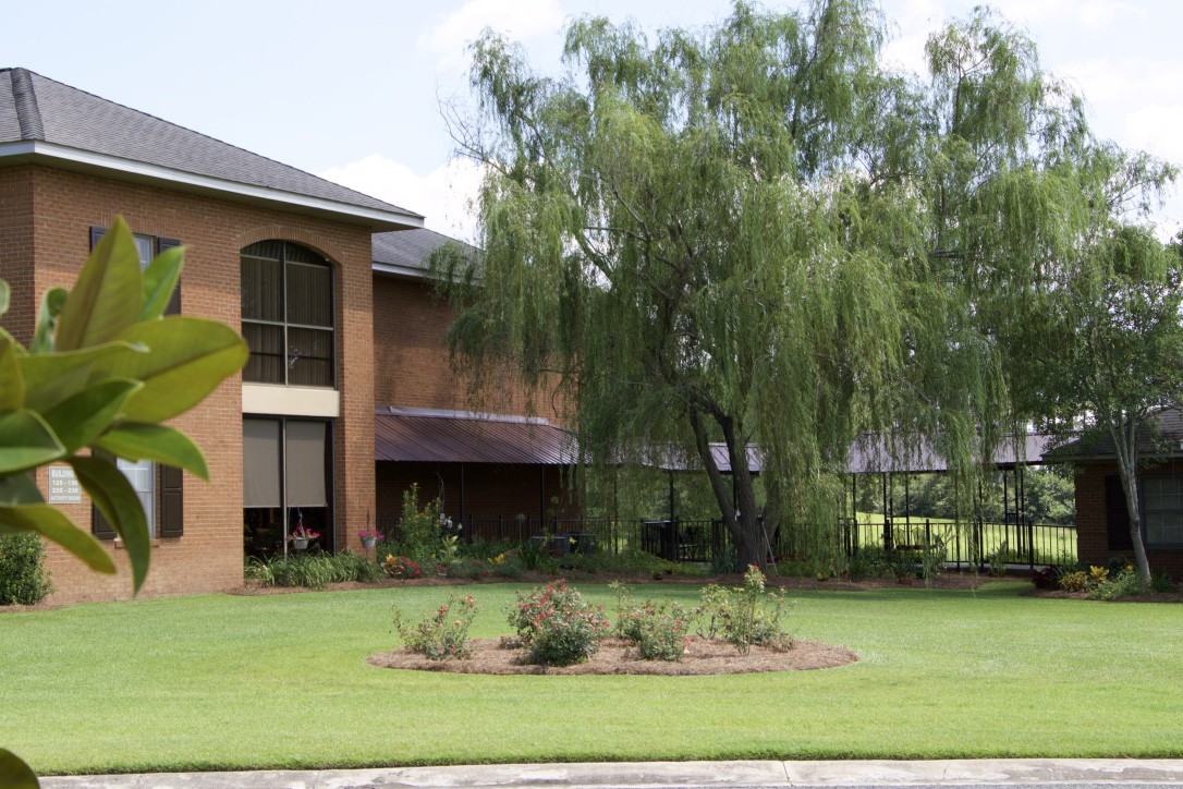 A modern brick building surrounded by trees and a well-maintained lawn.