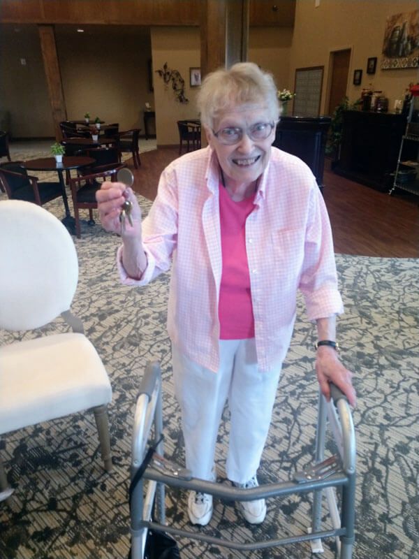 An elderly woman smiling while using a walker indoors.