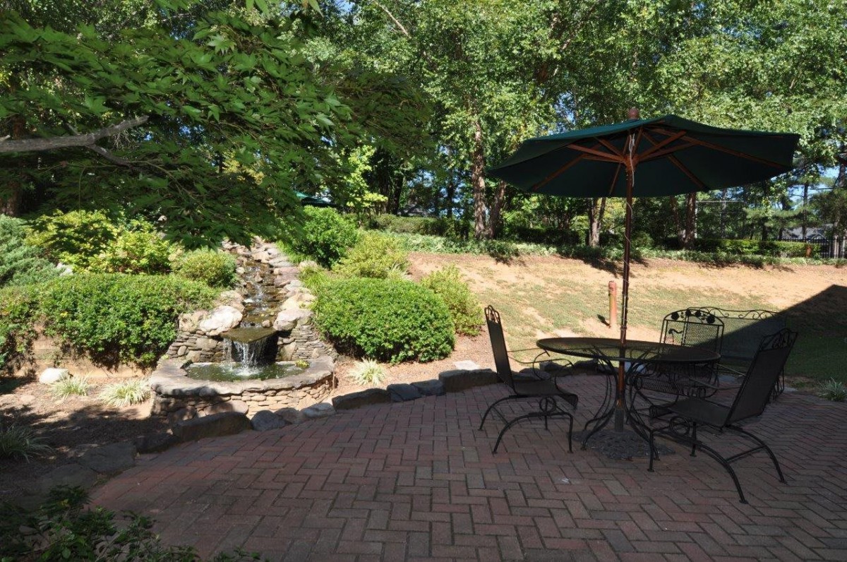 A tranquil garden patio with a seating area and a fountain surrounded by lush greenery.