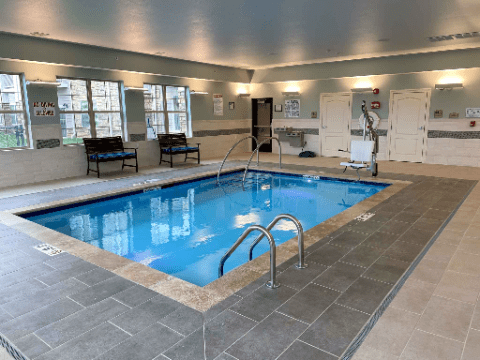 A well-lit indoor swimming pool with tile flooring and seating area.